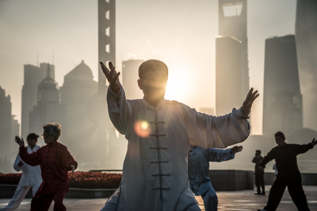 Älterer, asiatischer Mann praktiziert Tai Chi im Freien.
